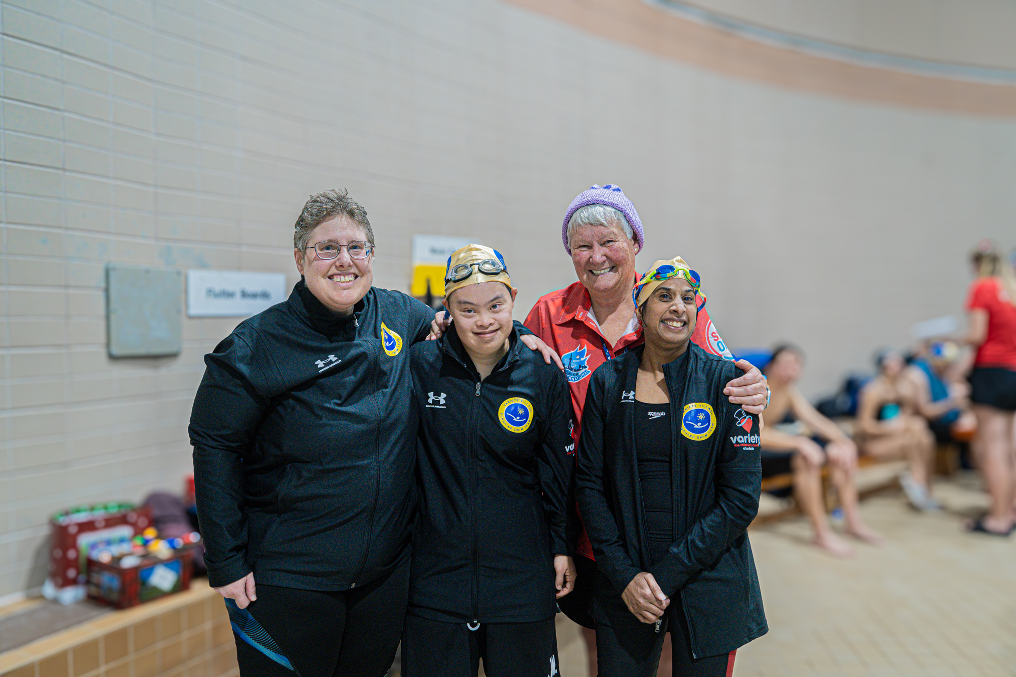 Three Sunshine Swim Team athletes and a referee pose together on the pool deck during a swim meet.