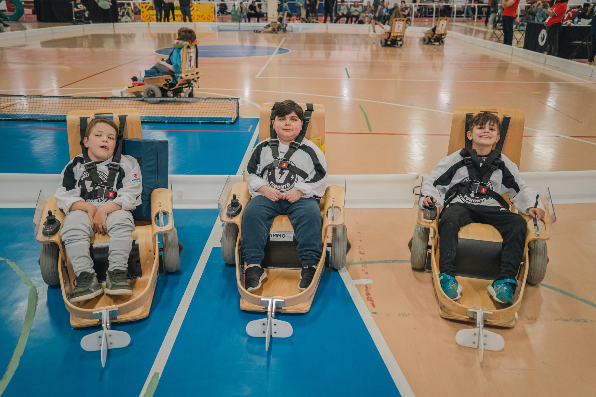 Three young VOLT Hockey athletes sit in sport chairs on an indoor court wearing team jerseys.