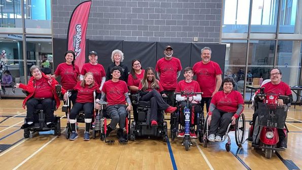Members of a boccia team and their coaches pose for a group photo on an indoor court.