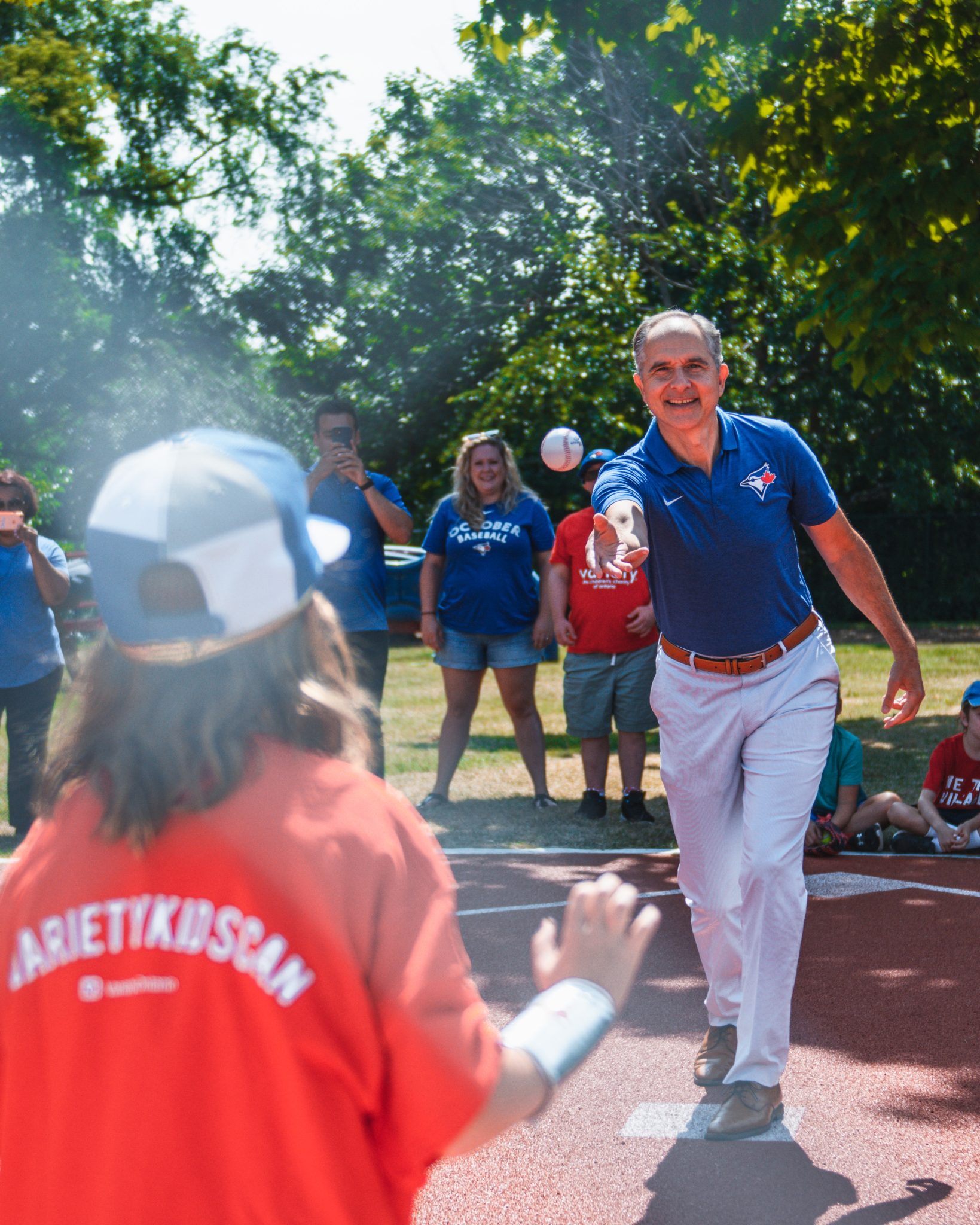 Person tosses a baseball to a child wearing a Variety Kid Can shirt during an accessible baseball event.