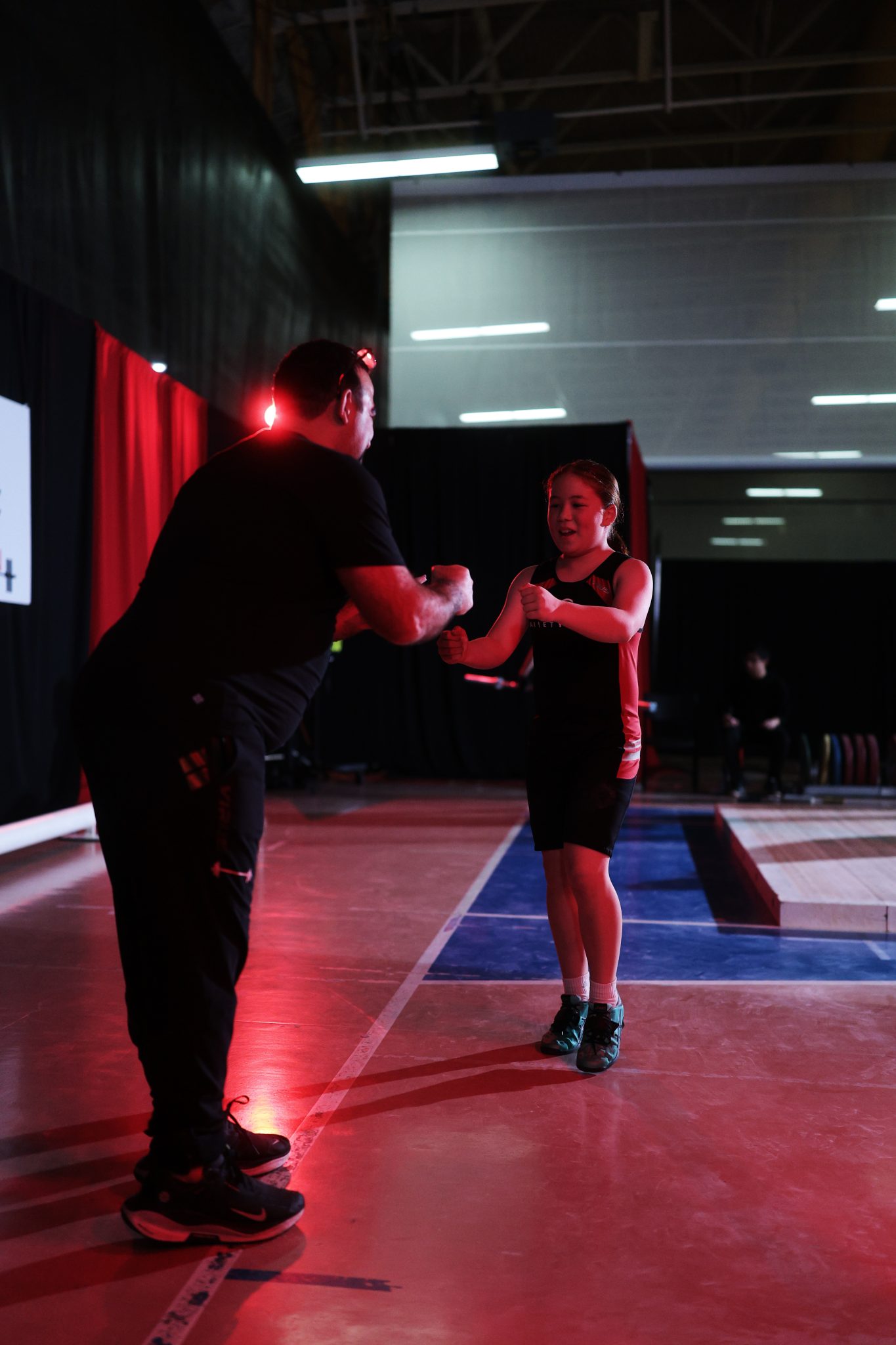 Coach and young weightlifter exchange a fist bump beside the competition platform after a successful lift.