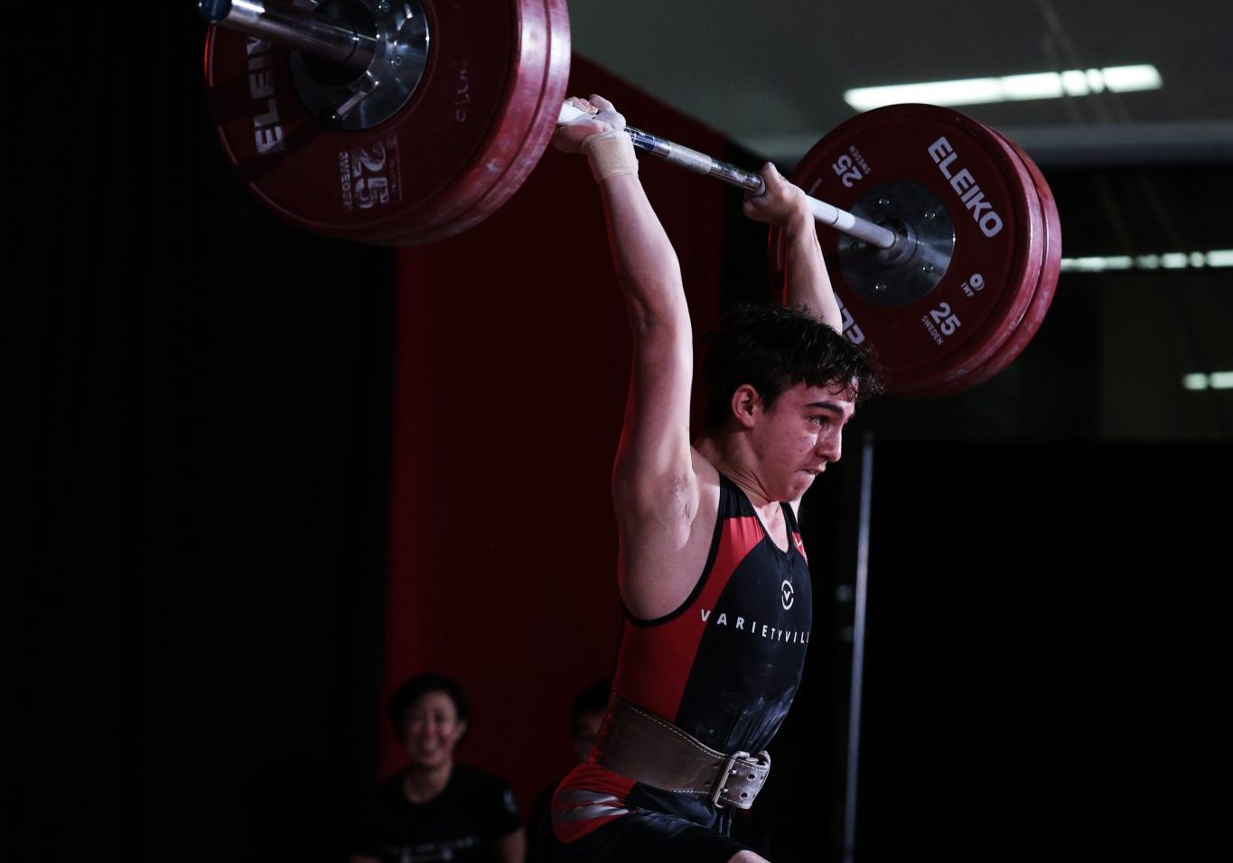 Athlete completes a split jerk with a heavily loaded barbell locked overhead on the competition platform.