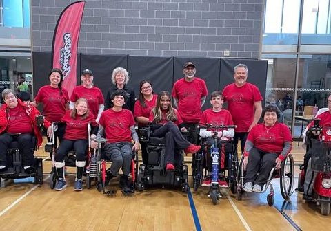 Members of a boccia team and their coaches pose for a group photo on an indoor court.